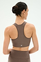 A person with dark hair in a bun is shown from the back, wearing the SPLITS59 Airweight Bra With Ruching in Lentil and matching leggings, both made from stretch fabric, against a plain light background.