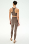 A person stands facing away, wearing SPLITS59′s Airweight High Waist 7/8 Pocket Legging in Lentil and a matching taupe spandex sports bra with white sneakers, against a plain light background.