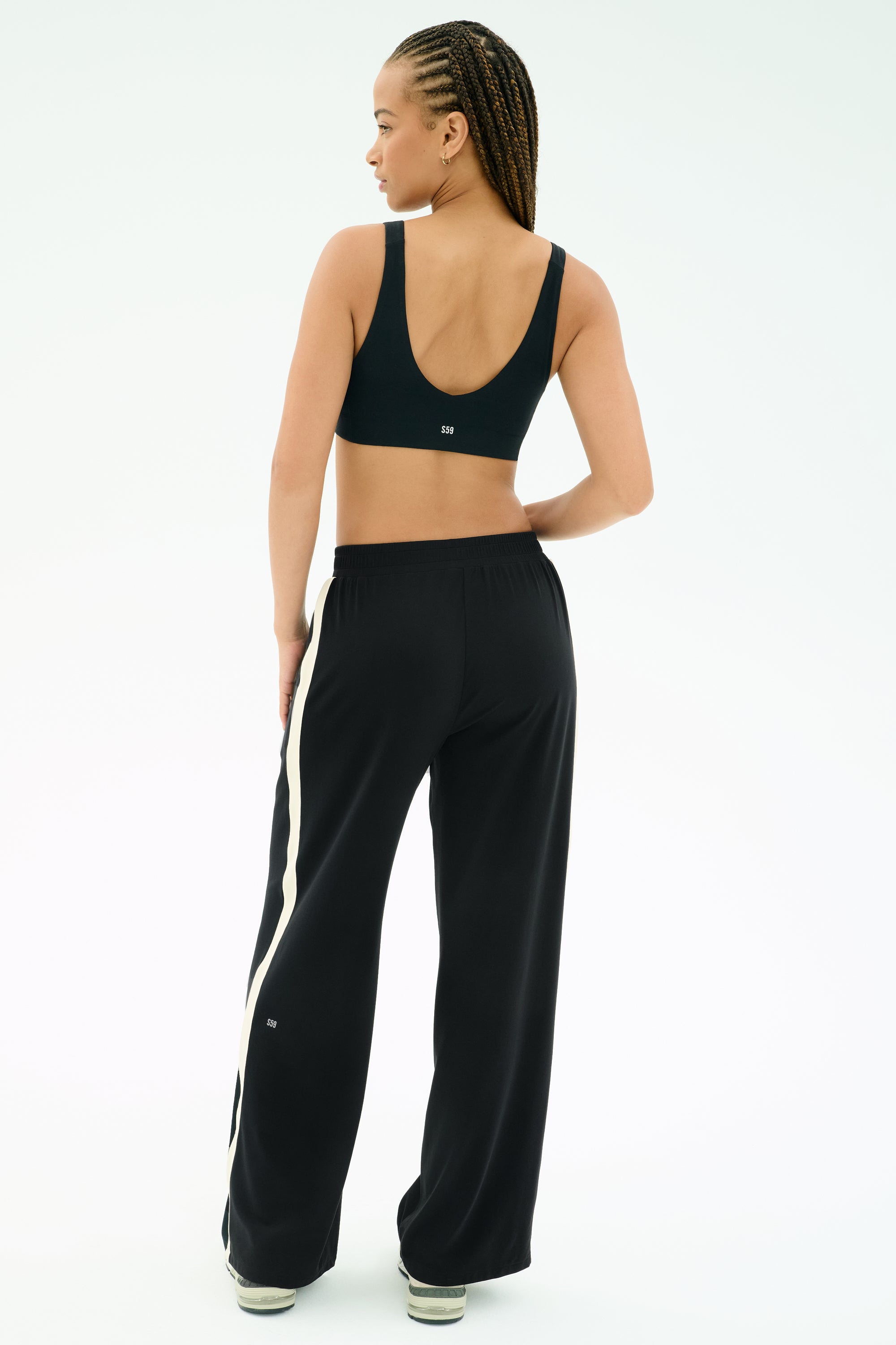 A person is seen from behind against a white background wearing the SPLITS59 Airweight Scoop Back Bra in black and wide-leg pants with a white side stripe.