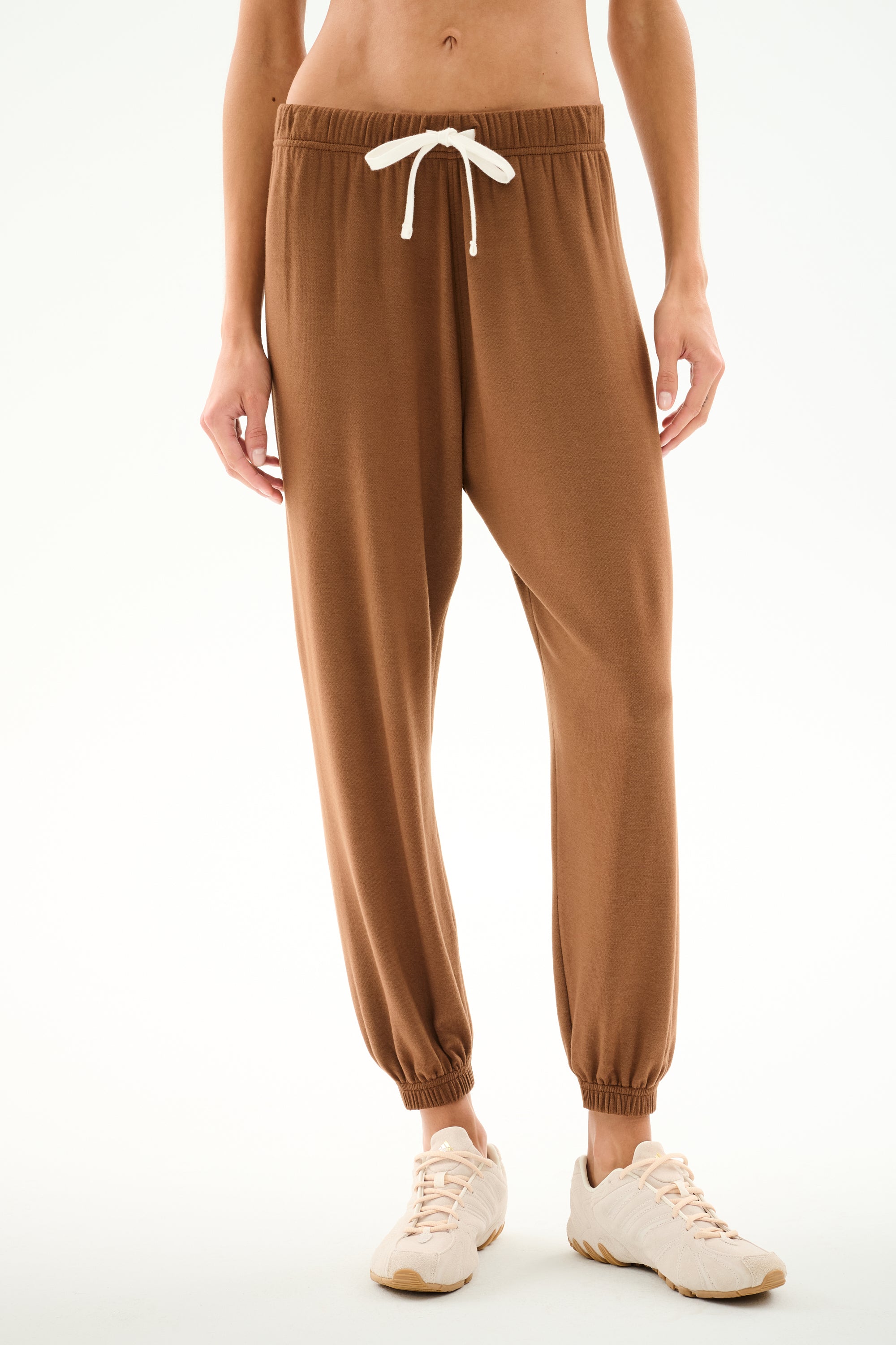 Person wears SPLITS59 Andie Oversized Fleece Sweatpant - Toffee with a white drawstring and beige sneakers, standing against a plain white background.