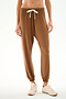 Person wears SPLITS59 Andie Oversized Fleece Sweatpant - Toffee with a white drawstring and beige sneakers, standing against a plain white background.