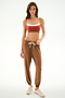 Woman in studio wears a red sports bra, SPLITS59 Andie Oversized Fleece Sweatpant - Toffee, and beige sneakers against a plain white background.