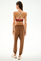 A woman faces away, wearing the Andie Oversized Fleece Sweatpant - Toffee by SPLITS59 with a crisscross sports bra and light sneakers against a plain white background.