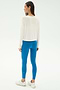 A woman faces away, wearing the SPLITS59 Djuna Long Sleeve - White, bright blue leggings, and white sneakers against a plain background—ideal for gym or outdoor workouts.