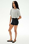 A woman stands against a white background wearing the SPLITS59 Djuna Oversized Crop Jersey Tee in Heather Grey, styled with black fitted shorts and black ballet flats.