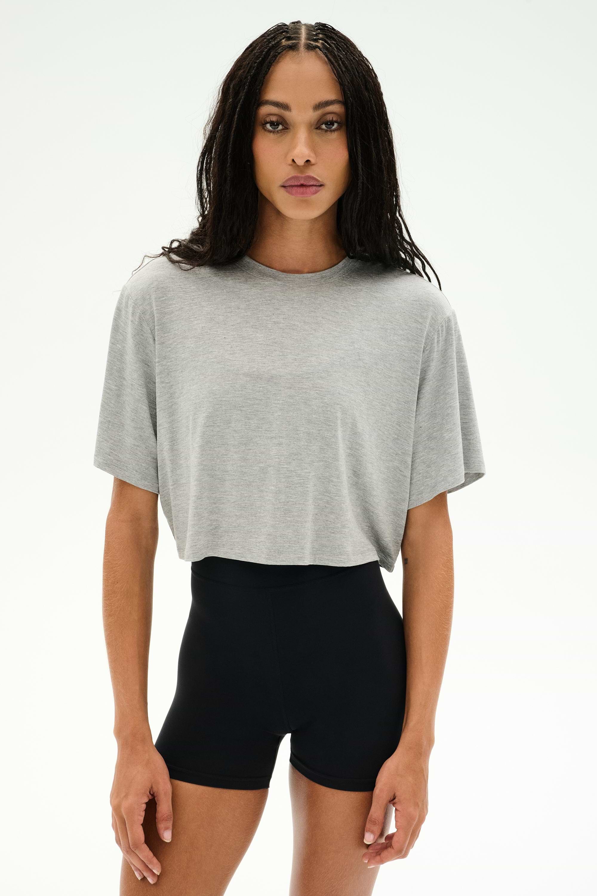 A woman stands facing forward against a plain white background, wearing the SPLITS59 Djuna Oversized Crop Jersey Tee in Heather Grey and high-waisted black shorts.
