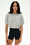 A woman stands facing forward against a plain white background, wearing the SPLITS59 Djuna Oversized Crop Jersey Tee in Heather Grey and high-waisted black shorts.