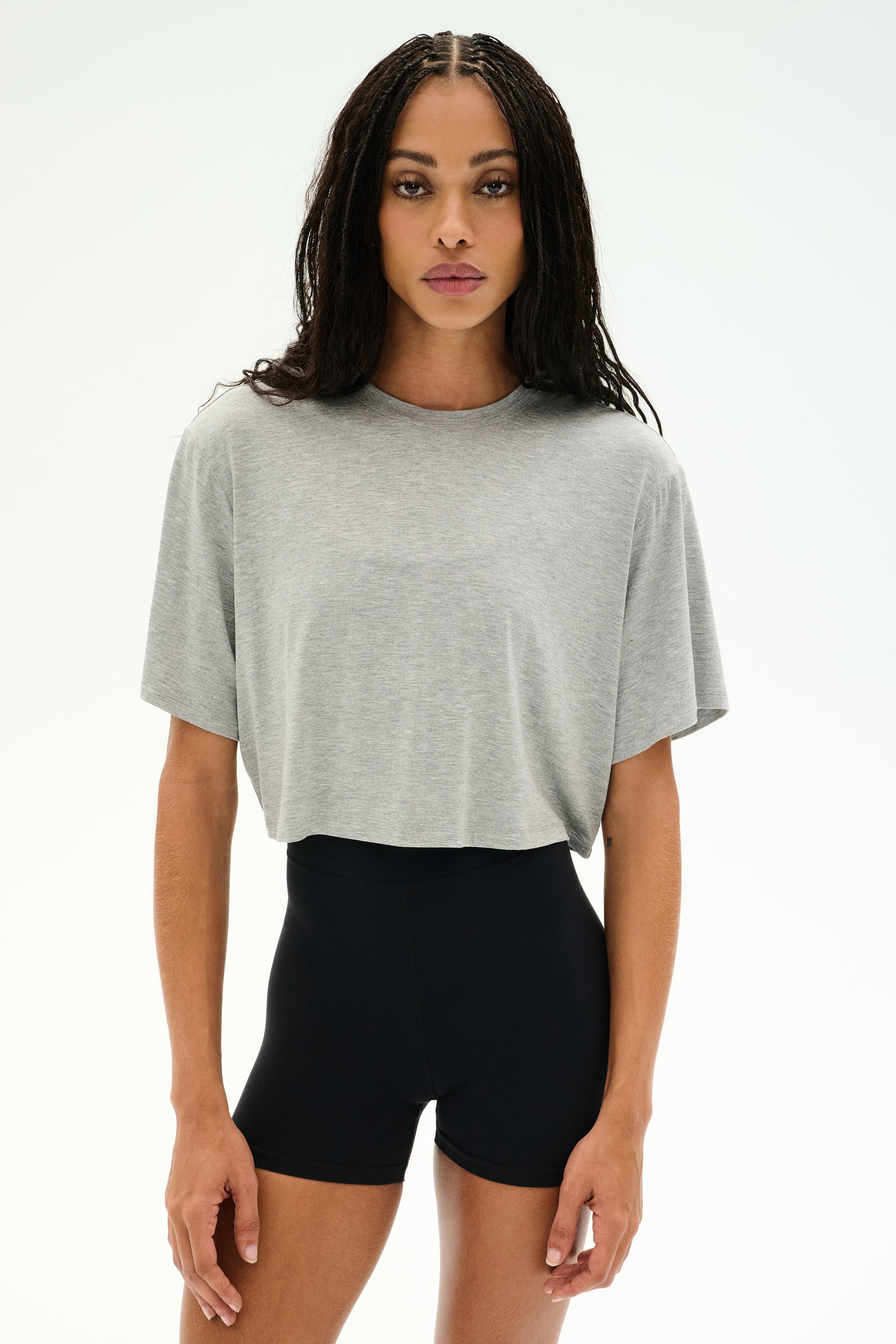 A woman stands facing forward against a plain white background, wearing the SPLITS59 Djuna Oversized Crop Jersey Tee in Heather Grey and high-waisted black shorts.