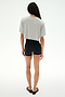 A person stands facing away against a white background, wearing SPLITS59's Djuna Oversized Crop Jersey Tee in Heather Grey, paired with black shorts and black flats.