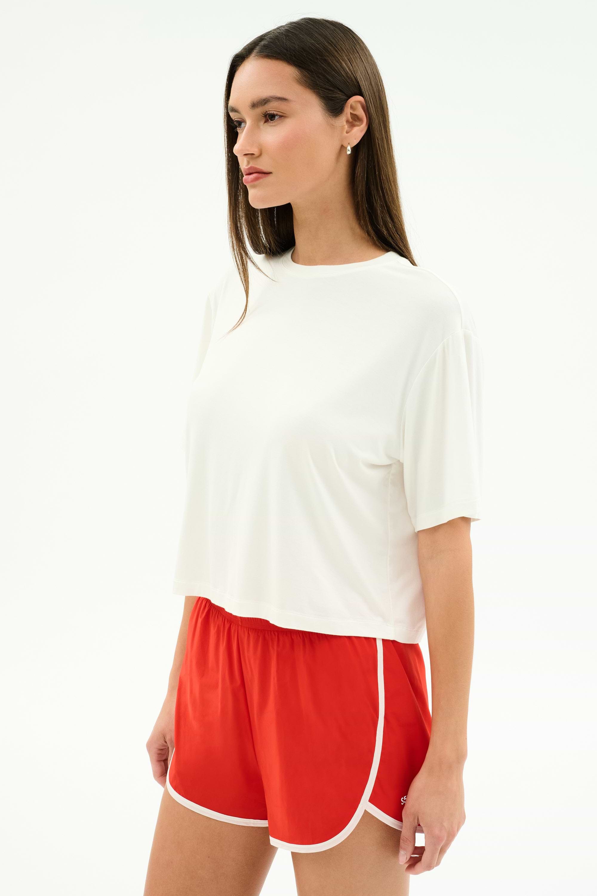 A woman stands slightly sideways against a plain white background, wearing the SPLITS59 Djuna Oversized Jersey Tee in White—ideal for outdoor workouts.
