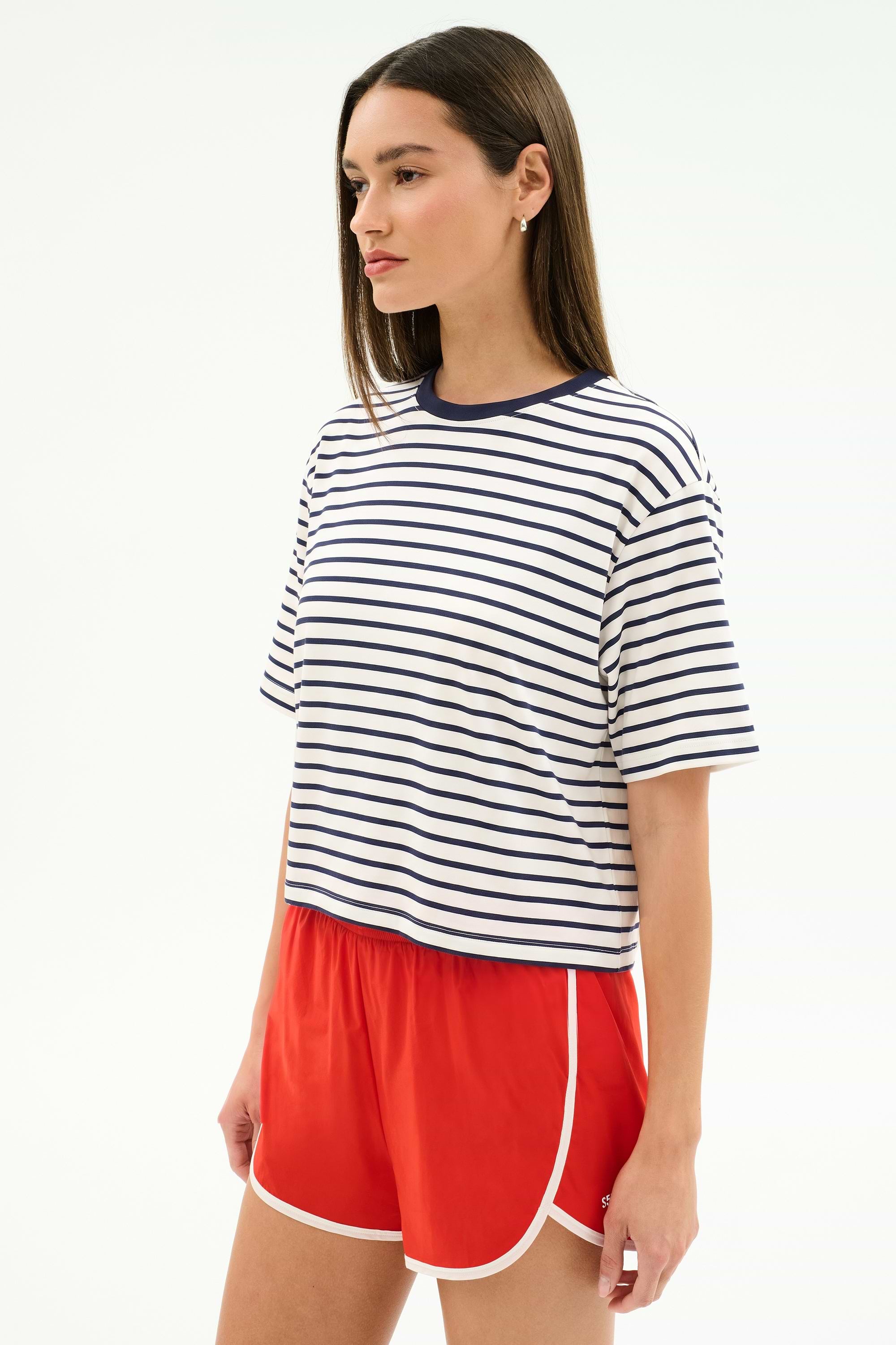 A woman wears the SPLITS59 Djuna Oversized Jersey Tee in White/Indigo Stripe with red athletic shorts, standing against a plain white background.