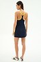 A woman stands with her back to the camera wearing the SPLITS59 Ella Airweight Dress in Indigo/Bright Yellow, paired with white sneakers featuring black stripes.