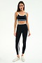 A woman faces forward in the SPLITS59 Eva Rigor Double Strap Bra in Black/Skylight, paired with high-waisted black leggings and white sneakers, against a plain white background.