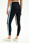 A person stands facing away, wearing SPLITS59 Sam High Waist Rigor 7/8 leggings in black/skylight with blue and white side stripes, paired with white athletic shoes against a plain background.