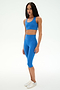 A person stands against a plain white background, wearing the SPLITS59 Airweight High Waist 16" Capri Legging in Classic Blue with a matching blue sports bra and white sneakers.