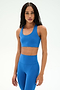 A woman wearing the SPLITS59 Sara Airweight Bra in Classic Blue, crafted from a comfortable spandex and nylon blend, stands against a plain white background.