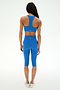A person stands with their back to the camera, wearing the SPLITS59 Airweight High Waist 16" Capri Legging in Classic Blue, paired with a matching blue sports bra, against a plain white background.