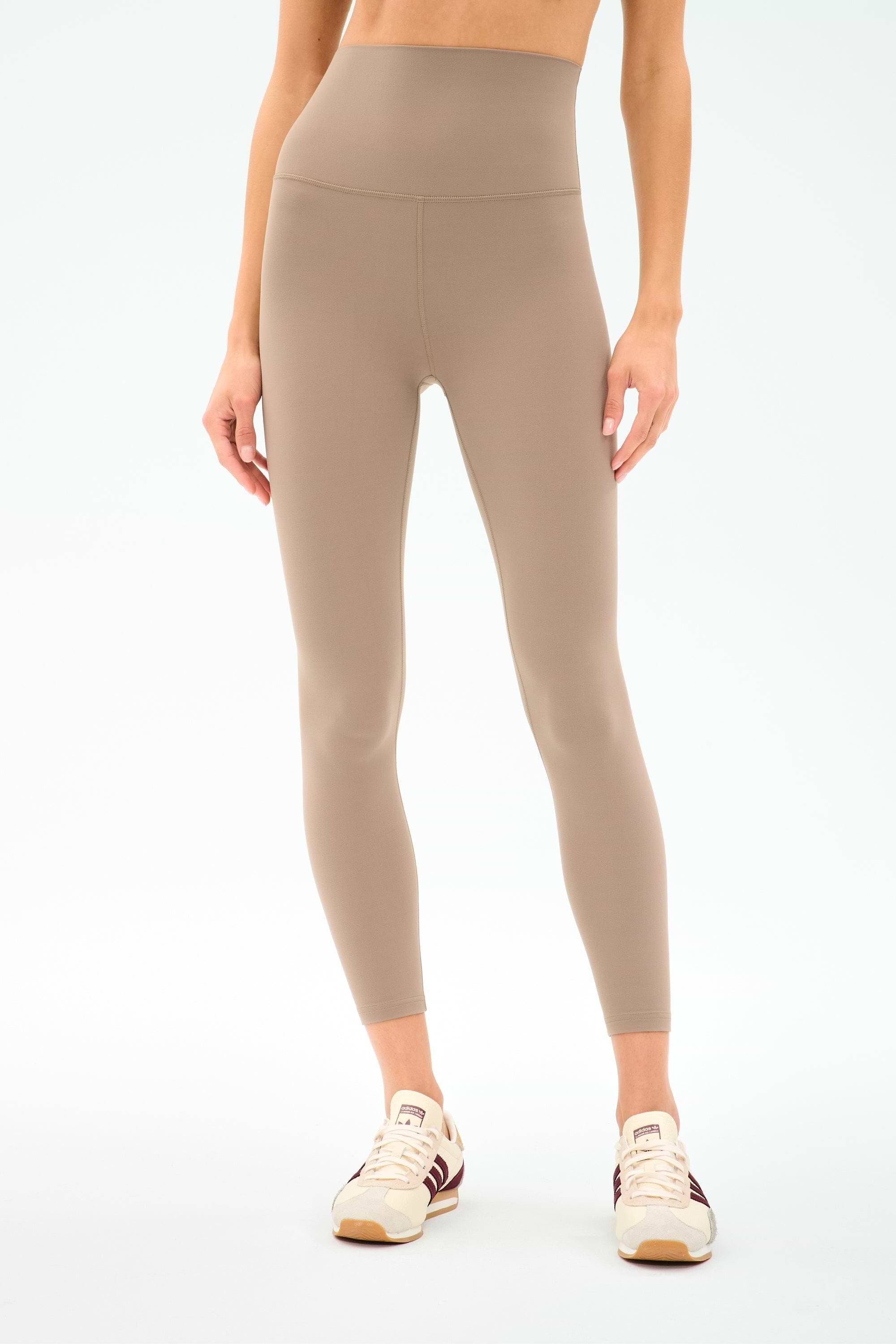 A person wearing SPLITS59 Airweight Super High Waist 7/8 leggings in Latte with cream sneakers, shown midriff to feet against a plain background—ideal for hot yoga thanks to the ultra luxe Airweight fabric.