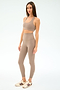 A woman poses against a white background wearing the SPLITS59 Airweight Super High Waist 7/8 leggings in Latte, paired with a taupe sports bra and beige sneakers featuring maroon stripes—an ideal outfit for hot yoga.