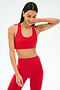 A woman wears the SPLITS59 Sara Airweight Bra in Pirate Red with matching high-waisted leggings, posing against a plain light background—ideal for hot yoga or Pilates.