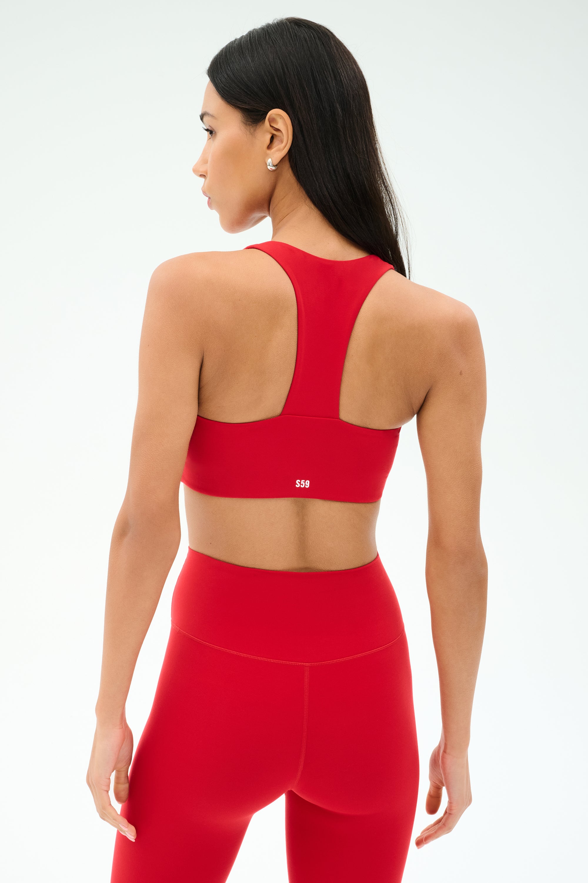 A woman, seen from the back against a light background, wears the SPLITS59 Sara Airweight Bra in Pirate Red with matching leggings—ideal activewear for Pilates or hot yoga.
