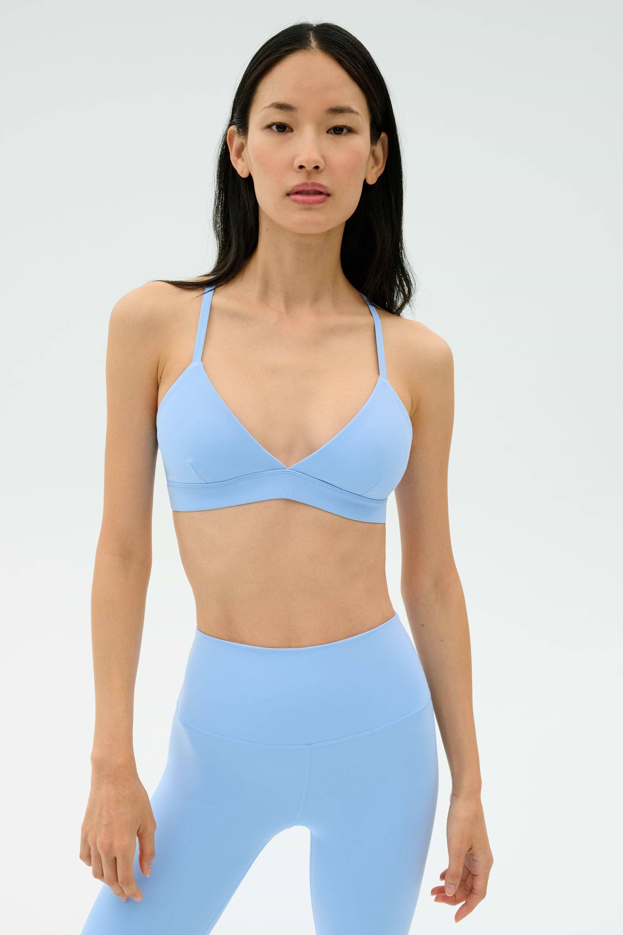 A woman stands against a plain background wearing the SPLITS59 Theo Rigor Bra in Skylight with matching high-waisted leggings.