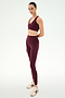 A person stands against a white background wearing the SPLITS59 Airweight Bra With Ruching in Dark Cherry, paired with matching leggings made from soft nylon spandex fabric and beige sneakers.