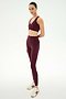 A person stands against a white background wearing the SPLITS59 Airweight High Waist 7/8 Pocket Legging in Dark Cherry and a matching sports bra set, paired with cream sneakers, posing with arms relaxed by their side.