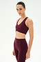 A person stands in profile against a plain, light background, wearing the SPLITS59 Airweight Bra With Ruching in Dark Cherry—a soft nylon-spandex sports bra—paired with matching high-waisted leggings.