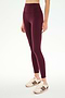 A person wearing SPLITS59 Airweight High Waist 7/8 Pocket Legging in Dark Cherry, paired with white sneakers featuring maroon stripes, stands against a plain white background.