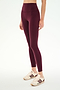A person wearing SPLITS59 Airweight High Waist 7/8 Pocket Legging in Dark Cherry, paired with white sneakers featuring maroon stripes, stands against a plain white background.