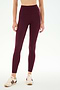 A woman stands against a plain white background, wearing SPLITS59’s Airweight High Waist 7/8 Pocket Legging in Dark Cherry and beige sneakers with maroon stripes.