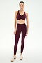 A woman stands against a white background, dressed in SPLITS59′s Airweight High Waist 7/8 Pocket Legging in Dark Cherry and a matching sports bra, paired with beige sneakers.