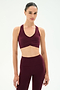 A woman wears the SPLITS59 Airweight Bra With Ruching in Dark Cherry, paired with matching high-waisted leggings, both crafted from soft stretch fabric for ultimate comfort, standing against a plain white background.