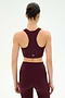 A person stands facing away, wearing the SPLITS59 Airweight Bra With Ruching in Dark Cherry and matching leggings, both crafted from smooth nylon spandex fabric, against a plain white background.