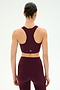 A person stands facing away, wearing the SPLITS59 Airweight Bra With Ruching in Dark Cherry and matching leggings, both crafted from smooth nylon spandex fabric, against a plain white background.
