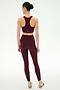 A person stands facing away, wearing the SPLITS59 Airweight Bra With Ruching in Dark Cherry along with matching leggings, both crafted from soft nylon spandex fabric, and pairs them with light-colored sneakers against a plain white background.