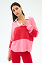 A woman wears the SPLITS59 Katie Fleece Rugby in Strawberry/Pirate Red, featuring color-block pink and red with a white collar, paired with red pants, against a plain light background.