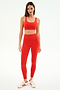 A woman stands against a plain white background wearing the SPLITS59 Airweight Rib Bra in Lotus Red, paired with matching ribbed leggings, ideal for hot yoga, and white sneakers with red stripes.