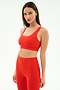 A woman wears the SPLITS59 Airweight Rib Bra in Lotus Red with matching high-waisted leggings, made from ribbed airweight fabric—ideal for hot yoga—posing against a plain white background.