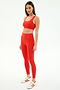 A woman poses against a plain background in the SPLITS59 Airweight Rib Bra - Lotus Red, paired with matching leggings and white sneakers with red stripes—an ideal set for hot yoga.