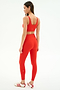 A woman faces away, wearing the SPLITS59 Airweight Rib Bra in Lotus Red with matching leggings and white Adidas sneakers with red stripes, set against a plain white background.