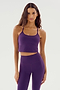 A woman with long hair stands against a plain background, wearing the SPLITS59 Airweight Crop in Black Currant and matching high-waisted leggings, both made of stretchy spandex.