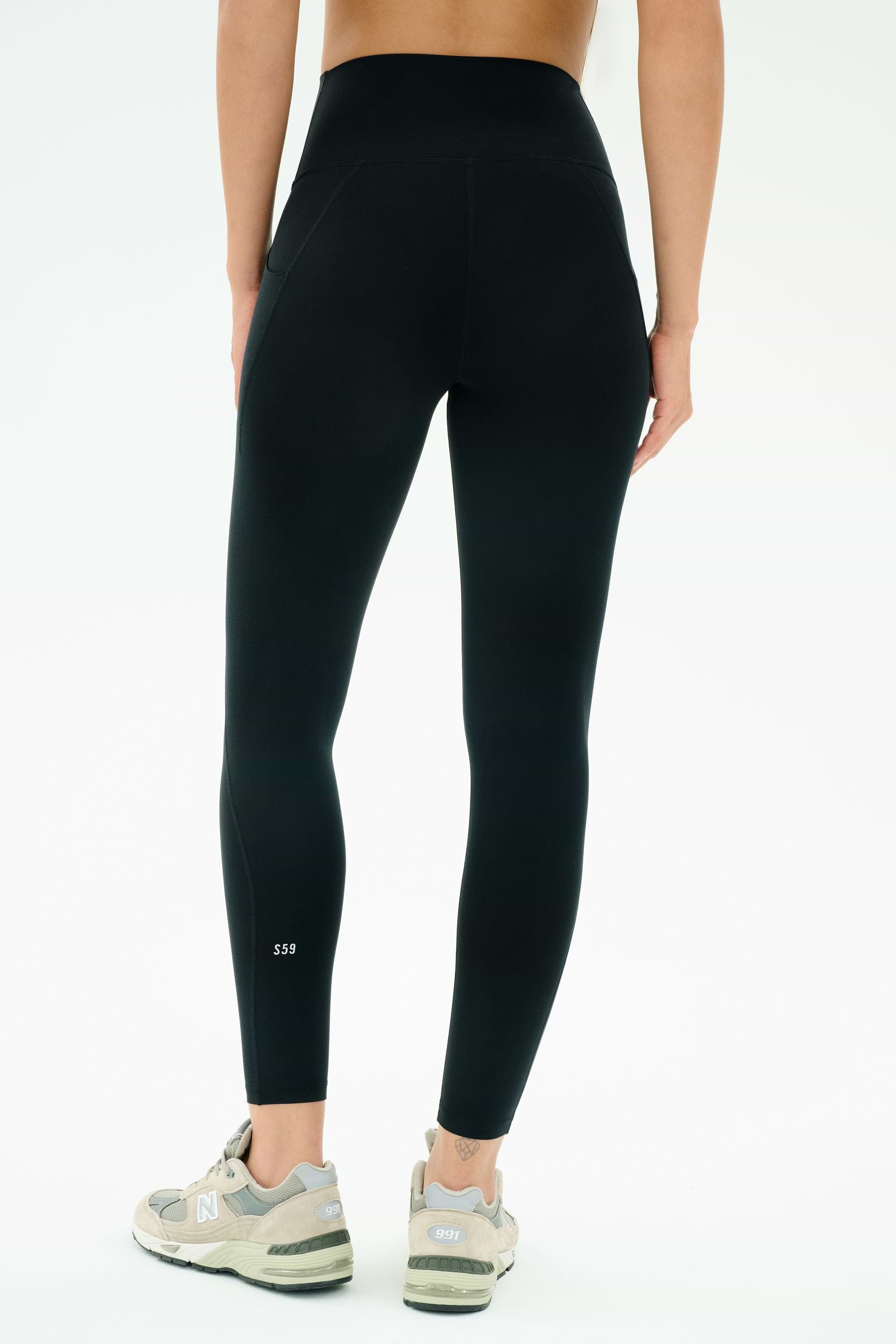 A person is shown from the back in SPLITS59 Airweight High Waist 7/8 Pocket Legging in black and grey New Balance sneakers, standing against a plain white background.