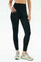 A person wears SPLITS59’s Airweight High Waist 7/8 Pocket Legging in black with beige New Balance sneakers, standing against a plain white background.