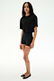 A person stands against a plain background wearing the SPLITS59 Djuna Oversized Crop Jersey Tee in black, paired with black fitted shorts and black flats.