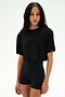 A person with long, braided hair wears the SPLITS59 Djuna Oversized Crop Jersey Tee in black and stretchy black high-waisted shorts, standing against a plain light background.