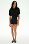 A person stands facing forward against a plain white background, wearing the SPLITS59 Djuna Oversized Crop Jersey Tee in black, paired with fitted black shorts and black flats.