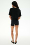 A person faces away, wearing the SPLITS59 Djuna Oversized Crop Jersey Tee in black with matching black shorts and flats, all set against a plain white background.