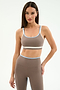 A woman stands against a plain background wearing the SPLITS59 Eva Rigor Double Strap Bra in Lentil/White, perfect for yoga or workouts, paired with matching high-waisted leggings.